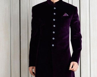 May include: A long, dark purple velvet coat with a mandarin collar and button closure. The coat has a tailored fit and is paired with dark blue pants and olive green shoes. A small purple pocket square is visible.