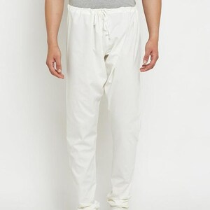 May include: White cotton trousers with a drawstring waist and a slim fit. The trousers are cuffed at the ankles.
