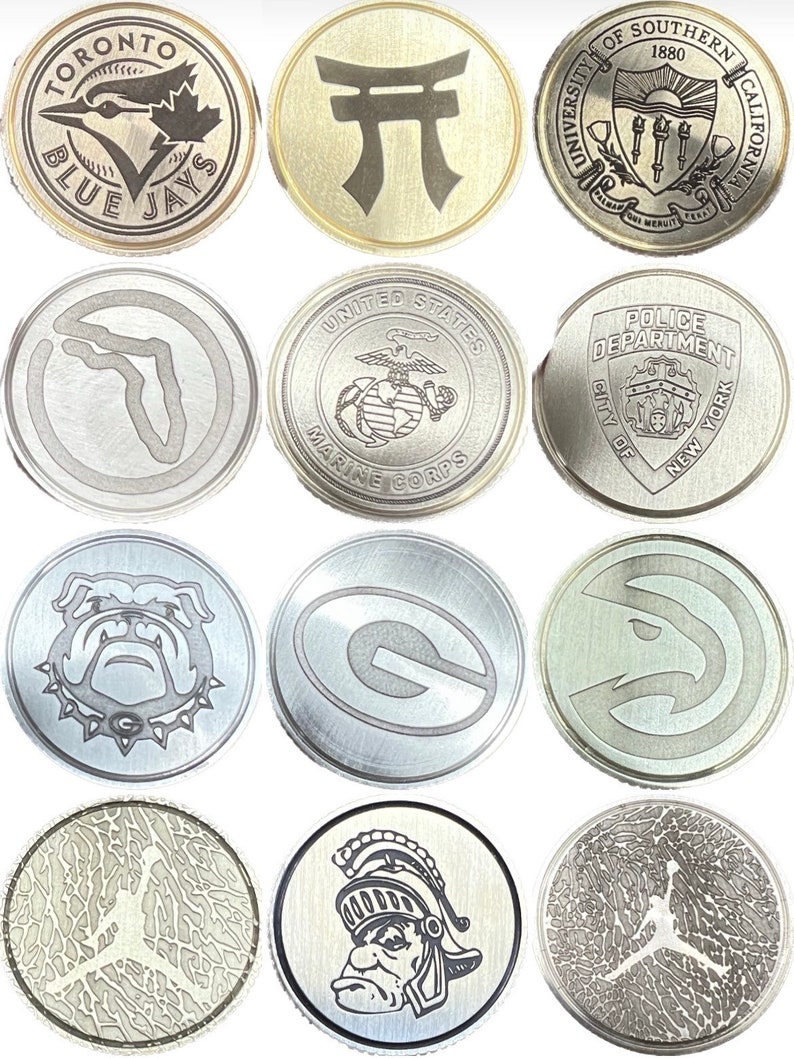 Puede incluir: Una colecci&oacute;n de monedas de metal plateado. Cada moneda presenta un dise&ntilde;o diferente, incluyendo logotipos de equipos deportivos, una puerta Torii japonesa, el emblema del Cuerpo de Marines de EE. UU. y el sello de la Universidad del Sur de California. Algunas monedas tienen texto como "TORONTO BLUE JAYS".