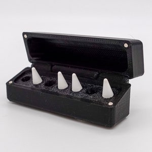 Può includere: Una custodia in plastica nera con un coperchio incernierato, aperta per rivelare cinque coni in plastica bianca all'interno.