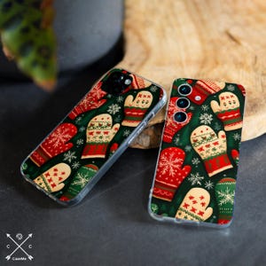 May include: Two clear phone cases with a festive pattern of red, green, and cream-colored mittens and snowflakes on a dark green background. The cases are on a wooden surface, with a dark gray background.