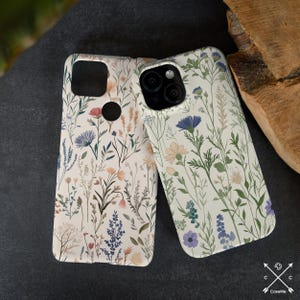 May include: Two phone cases with a floral pattern. The cases are white with a light pink, blue, and green floral design. The cases are for a phone with a triple camera lens.