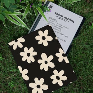 May include: A black tablet case with a cream-colored daisy pattern rests on grass next to an open e-reader. The e-reader displays the text "FRIDAY MEETING" and an agenda. The CaseMe logo is in the upper right corner.