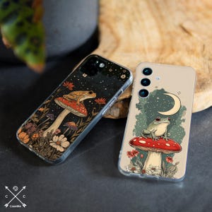 May include: Two phone cases with a whimsical design featuring frogs sitting on mushrooms in a forest setting. One case has a green frog on a red mushroom with a crescent moon in the background. The other case has a brown frog on a red mushroom with a starry night sky in the background.