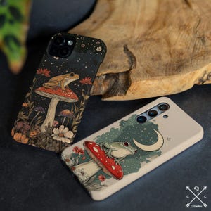 May include: Two phone cases with a whimsical design featuring frogs sitting on mushrooms. One case has a dark background with a starry sky and a green frog, while the other has a light background with a crescent moon and a brown frog.