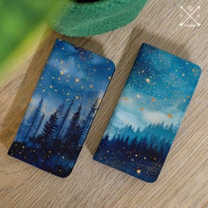 May include: Two phone cases with a starry night design. The cases feature a dark blue and teal color scheme with gold stars and silhouettes of pine trees. The cases are rectangular and appear to be made of a durable material.
