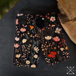 May include: A black phone case with a floral pattern featuring pink, red, orange, and white flowers on a black background. The case has a cutout for the camera lens.