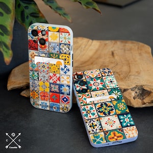 May include: Two white phone cases with a colorful tile pattern. The cases have a built-in card holder.