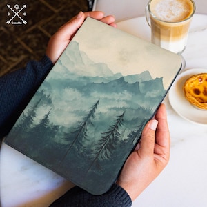 May include: A tablet case featuring a watercolor landscape of mountains and evergreen trees in shades of blue and green. The case has a black border and is held in hands. The brand name "CaseMe" is visible in the upper left corner.