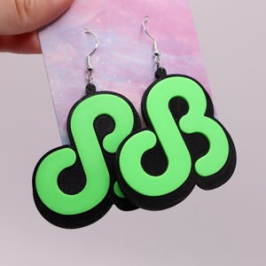 May include: A pair of green and black dangle earrings shaped like the letter "S" with a silver hook.