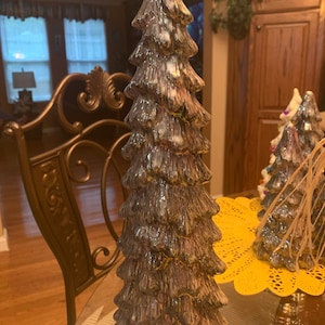 May include: A ceramic Christmas tree decoration with a white and brown glaze. The tree is tall and slender with a pointed top. It has a layered design with multiple tiers.
