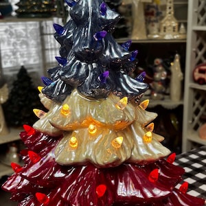 May include: A ceramic Christmas tree in red, white, and blue, with a star topper. The tree is illuminated with red, yellow, and blue lights. The tree is approximately 12 inches tall and is a festive holiday decoration.