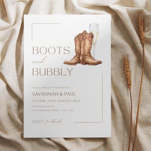 Puede incluir: Una tarjeta de invitación blanca con texto marrón que dice "Boots and Bubbly". La invitación es para una despedida de soltera para Savannah y Paul. La tarjeta presenta una ilustración de acuarela de un par de botas de vaquero marrones y una copa de champán.