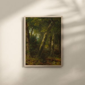 May include: A framed landscape painting depicting a forest scene. The artwork features tall trees with green foliage and dappled sunlight. The painting has a natural, vintage aesthetic, suitable for home decor.