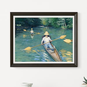 May include: A framed art print depicts a serene river scene. Two people in straw hats row wooden boats with yellow oars on a turquoise-colored river. Lush green trees line the riverbanks, and the artwork is framed in a dark brown frame.