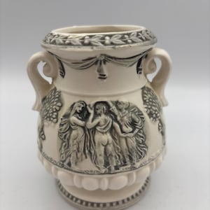 May include: Cream-colored ceramic vase with two handles and a detailed relief design. The vase features a classical scene with figures and decorative elements, with a gray and white color scheme.
