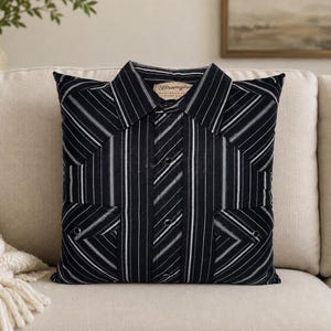 May include: A square throw pillow constructed from a black and white striped button-down shirt. The pillow features a pointed collar, a central button placket with visible metal snaps, and two chest pockets with flaps. A Wrangler brand label is visible.