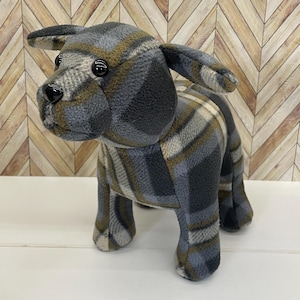 May include: A plush dog doorstop in a gray and brown plaid pattern. The dog is standing on all four legs and has black button eyes.