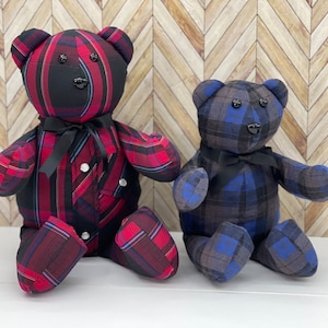 May include: Two stuffed teddy bears made from plaid fabric. The larger bear features a red, black, and blue plaid pattern with a black satin ribbon around its neck. The smaller bear has a blue, grey, and black plaid pattern with a black ribbon.