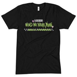 Op de afbeelding: Zwart T-shirt met groene tekst die "I Survived Wind We Were Young" luidt, met roze bloemenafbeeldingen en de tekst "October 22, 2022 Las Vegas Festival Grounds" in wit.