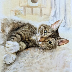 May include: A watercolor painting of a brown tabby cat with white paws lying down. The cat has dark stripes, green-yellow eyes, and long white whiskers. The background features a soft, light-colored wash with a faint outline of a cat tree.