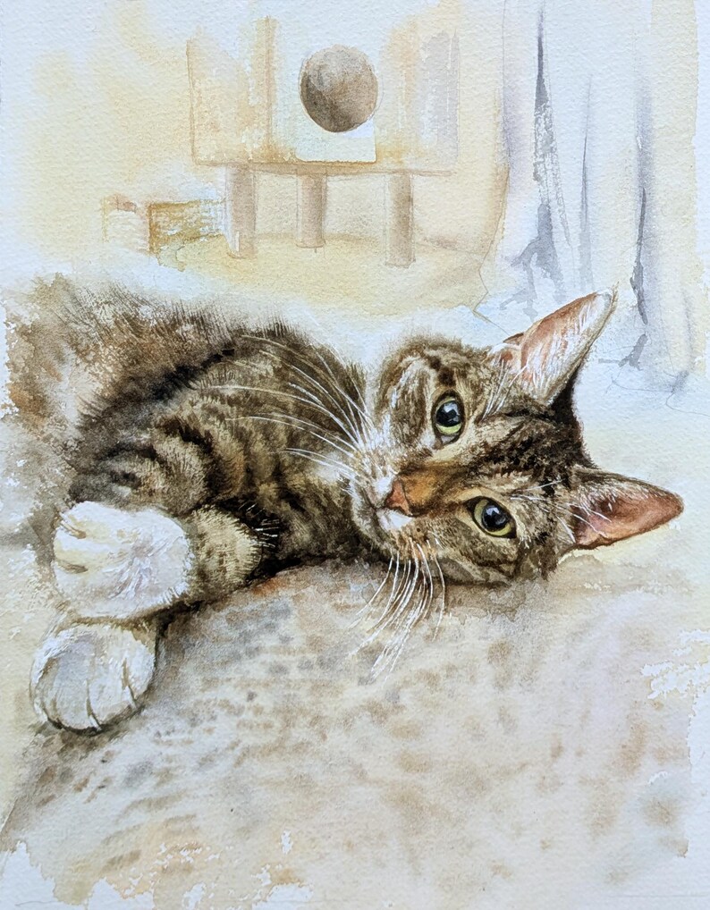 May include: A watercolor painting of a brown tabby cat with white paws lying down. The cat has dark stripes, green-yellow eyes, and long white whiskers. The background features a soft, light-colored wash with a faint outline of a cat tree.