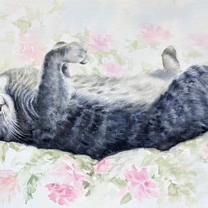 May include: A watercolor painting of a grey tabby cat lying on its back with its paws curled inward. The cat has dark grey stripes, white whiskers, and green eyes. It is positioned against a soft, light background featuring pale pink flowers.