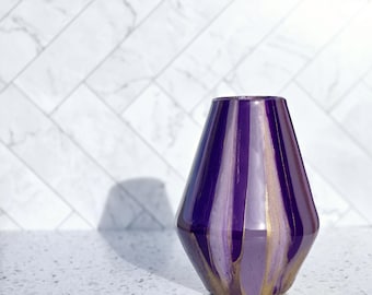 May include: Purple and gold iridescent vase with a geometric shape. The vase is made of glass and has a shiny finish.