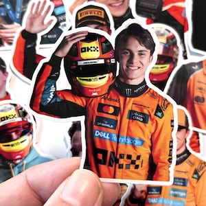 May include: A sticker featuring a Formula 1 driver in an orange racing suit holding a helmet. The helmet is red and black with the OKX logo. The sticker has the Dell Technologies and Cisco logos.