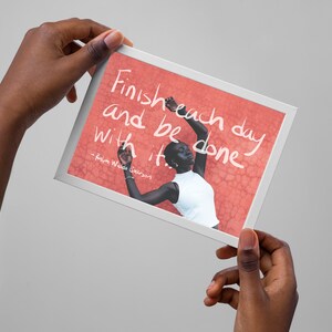 Op de afbeelding: Een ingelijst print met een citaat dat luidt: "Maak elke dag af en wees er klaar mee." - Robin Williams. De print toont een foto van een persoon met een donkere huidskleur die voor een rode muur staat.