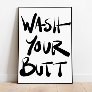 May include: A black and white framed print with the text "WASH YOUR BUTT" written in a bold, brushstroke font.
