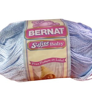 May include: A ball of light blue Bernat Softee Baby yarn. The label features a pink teddy bear and the text "Bernat Softee Baby". The label also states "Free Pattern on Label". This yarn is suitable for baby projects.