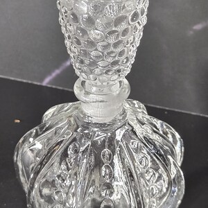 May include: A clear glass decanter featuring a rounded body with vertical fluted panels and a textured hobnail pattern. The matching glass stopper has a rounded top with a prominent hobnail design, fitting securely into the narrow neck.