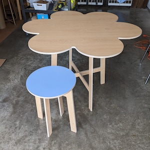 May include: A light blue round table with a wooden base and a flower-shaped wooden table with a light wood finish.