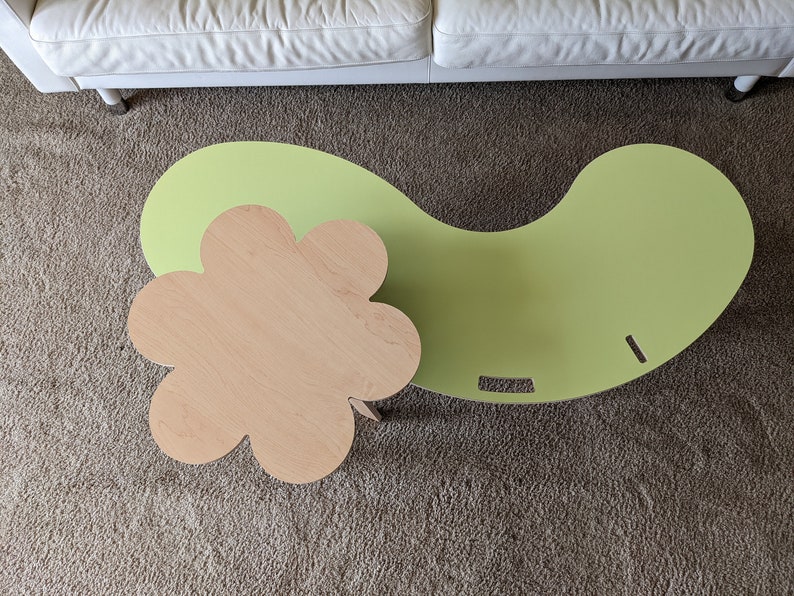 May include: A green and natural wood coffee table set with a unique flower-shaped top and a curved, kidney-shaped base.