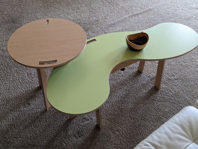 May include: A green and natural wood coffee table with a unique, organic shape. The table has a smaller round table attached to it, which can be used as a side table or a tray.