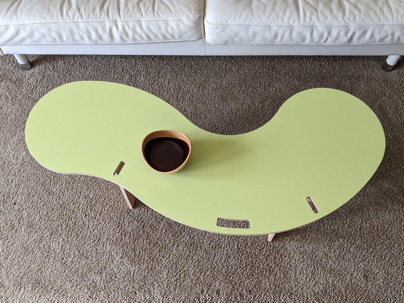 May include: A light green, kidney-shaped table with rounded edges and wooden legs. A small brown bowl sits on the table.