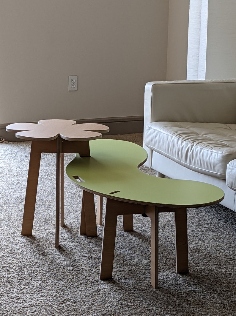 May include: Two wooden tables with unique shapes. The larger table is green and shaped like a kidney bean. The smaller table is brown and shaped like a flower. Both tables have four legs.