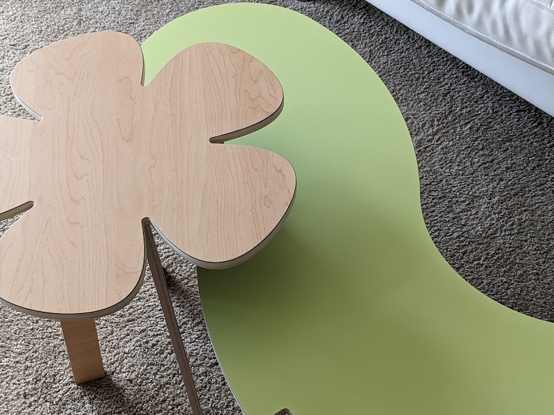 May include: A light green and natural wood coffee table with a unique clover-shaped top. The table has a modern, organic design.