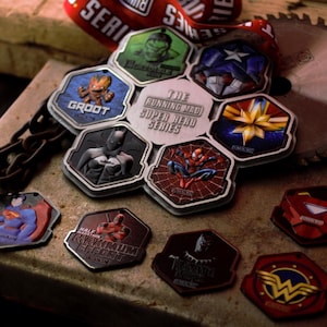 May include: A selection of superhero medals, showcasing characters such as Groot, Batman, and Spider-Man. The hexagonal medals display detailed character designs and the text "THE RUNNING MAD SUPER HERO SERIES". The medals are in various colours, including red, blue, and green.