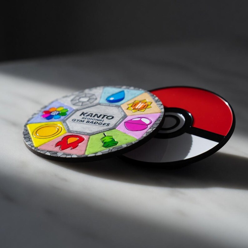 以下が含まれることがあります： 赤と白のPokeballと、カラフルなカントー地方ジムバッジのコレクション。バッジは円形に配置され、それぞれがユニークなデザインと色を持っています。「KANTO REGIONAL GYM BADGES」の文字がバッジに表示されています。