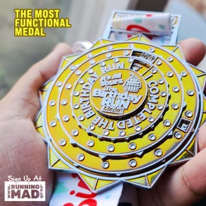 May include: A gold-colored medal with a white cupcake design and the text "It's All Yours the Birthday Run Medal" on the front. The medal is surrounded by a silver ring with the text "Completed the Birthday Run" on the back.