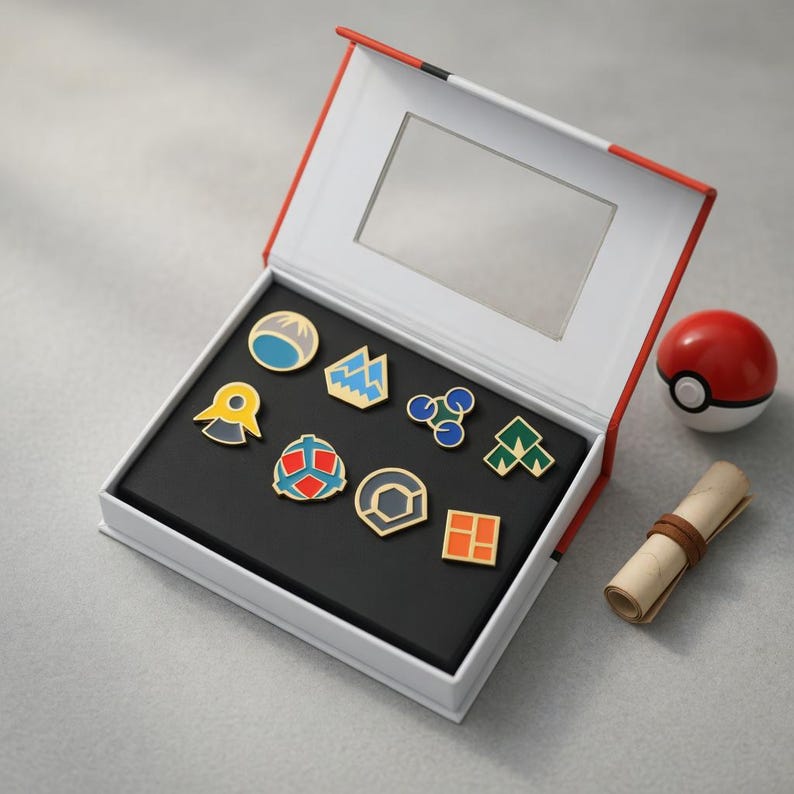 May include: A collection of eight colourful enamel pins displayed inside an open white and red box. The pins feature various geometric shapes and symbols in blue, yellow, orange, and green. Beside the box sits a red and white sphere and a small scroll.
