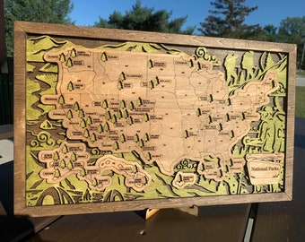 Puede incluir: Un mapa de madera de los Estados Unidos con un diseño en relieve que muestra la ubicación de todos los Parques Nacionales. El mapa está enmarcado en un marco de madera oscura y tiene un fondo marrón. El texto "National Parks" es visible en la esquina inferior derecha del mapa.
