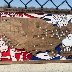May include: A wooden map of the United States with the location of all Major League Baseball stadiums marked. The map is surrounded by a baseball-themed design, including a baseball glove, a baseball bat, and a baseball player. The text "There are only two seasons: winter and baseball" is written at the top of the map. The text "Play Ball!" is written at the bottom of the map.
