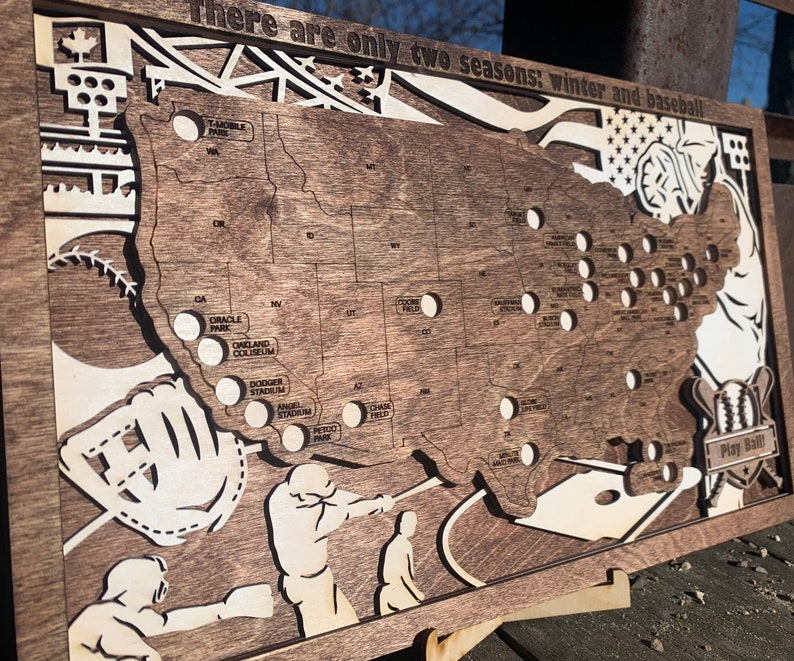May include: A wooden map of the United States with the location of all Major League Baseball stadiums marked. The map is decorated with baseball-themed imagery, including a baseball glove, a bat, and a baseball. The text "There are only two seasons: winter and baseball" is printed at the top of the map.