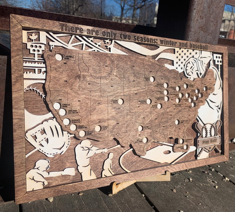 May include: A wooden map of the United States with a baseball theme. The map shows the locations of major league baseball stadiums. The text "There are only two seasons: winter and baseball" is printed at the top of the map. The map is framed in a dark wood frame.