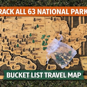May include: Wooden map of the United States with the text "Track All 63 National Parks" and "Bucket List Travel Map". The map is engraved with state outlines and tree-shaped markers. A small bag of tree markers is included.