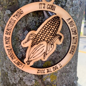 Puede incluir: Adorno de madera con dise&ntilde;o de mazorca de ma&iacute;z y las frases "It's corn", "A big lump with knobs", "It has the juice" y "I can't imagine a more beautiful thing" grabadas. Incluye cinta plateada.