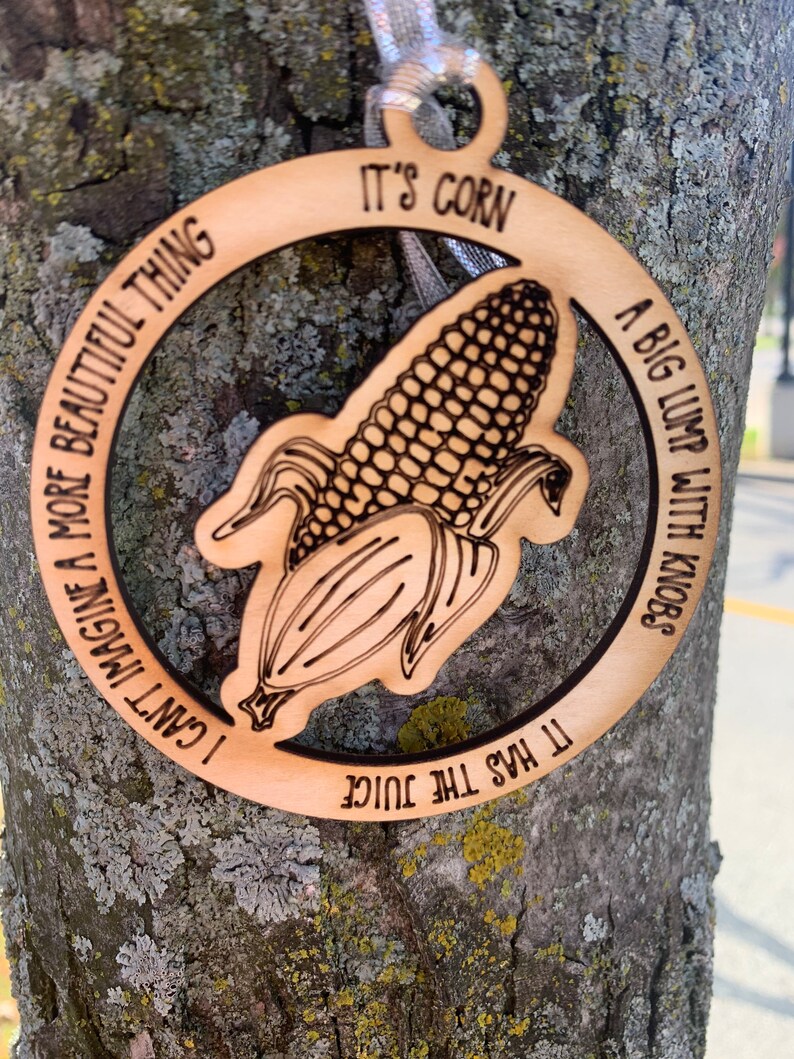 Puede incluir: Adorno de madera con dise&ntilde;o de mazorca de ma&iacute;z y las frases "It's corn", "A big lump with knobs", "It has the juice" y "I can't imagine a more beautiful thing" grabadas. Incluye cinta plateada.